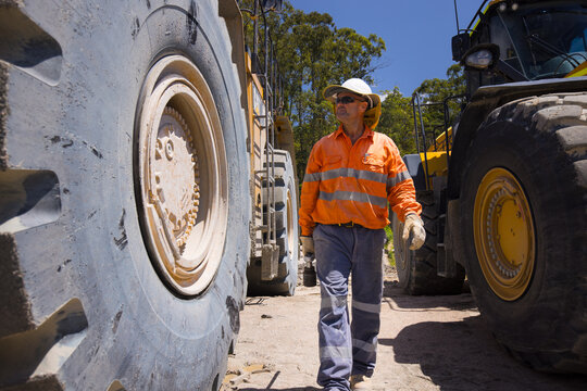 Man walking in between the massive wheels of payloader dump trucks