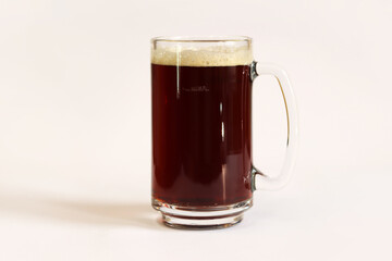 Kvass in a glass, light background. Glass of dark beer or kvass with foam in a glass on a light gray background. Traditional beer mug with a handle. Close-up on a glass with a cool tasty drink