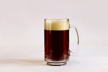 Kvass in a glass, light background. Glass of dark beer or kvass with foam in a glass on a light gray background. Traditional beer mug with a handle. Close-up on a glass with a cool tasty drink