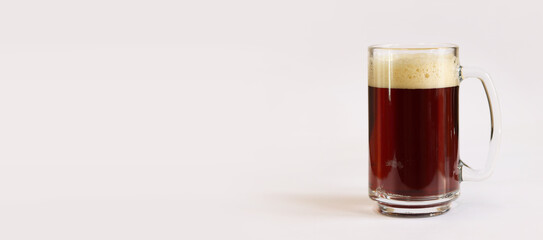 Kvass in a glass, light background. Glass of dark beer or kvass with foam in a glass on a light gray background. Traditional beer mug with a handle. Close-up on a glass with a cool tasty drink