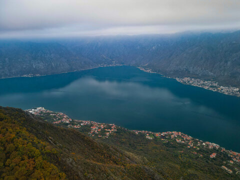 Aerial view of autumn mountain ridge with yellow trees under moody cloudy sky, blue mist and fog over Vrmac mountain in Montenegro.
