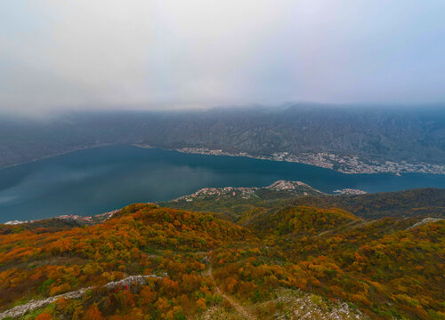Aerial view of autumn mountain ridge with yellow trees under moody cloudy sky, blue mist and fog over Vrmac mountain in Montenegro.