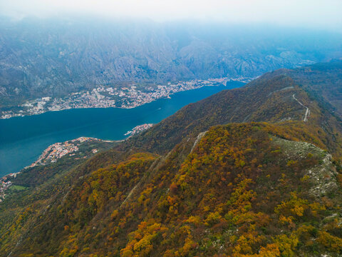 Aerial view of autumn mountain ridge with yellow trees under moody cloudy sky, blue mist and fog over Vrmac mountain in Montenegro.