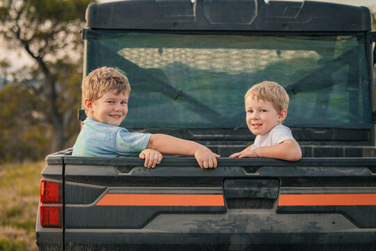 Two little boys sitting in back of off-road buggy on farm