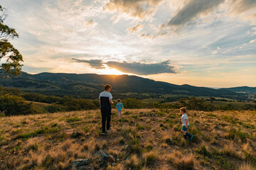 Teenager and two little boys exploring hilltop in regional New South Wales at sunset