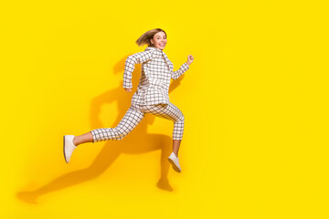 Full size photo of pretty young girl running hurry black friday wear trendy white checkered outfit isolated on yellow color background