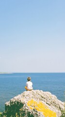 Serene Coastal Photo: Person Contemplatively Sitting on Rock, Ocean View. AI Generated