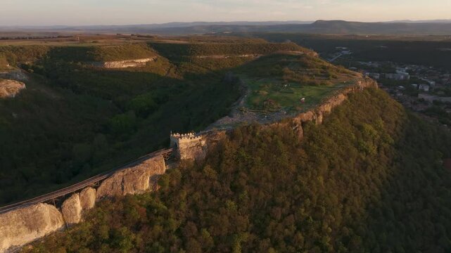 Aerial view of Ovech Fortress on a cliff during sunset surrounded by greenery, Provadia, Bulgaria.