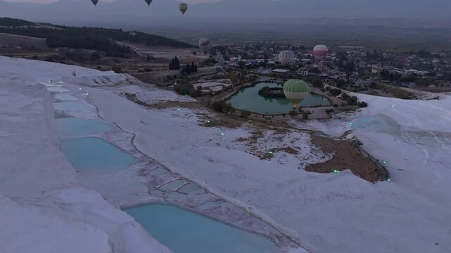 Aerial view of travertines of Pamukkale at sunrise with hot air balloons, Pamukkale, Turkey.