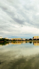 Obraz premium View of the city on the embankment with a gloomy evening sky, with rain clouds and reflection of buildings in the water.