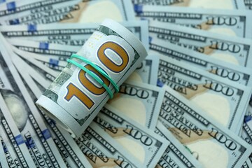 Fototapeta premium Roll of hundred dollar bills USD banknotes lies on big amount of united states money