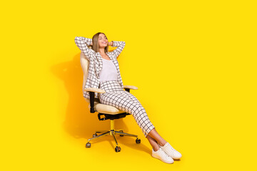 Confident woman in suit relaxing in office chair against vibrant yellow background, showcasing a blend of elegance and professional charm.