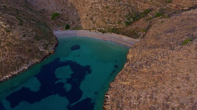 Aerial view of Vathi Beach at sunrise with tranquil turquoise water and rocky hills, Lagia, Greece.