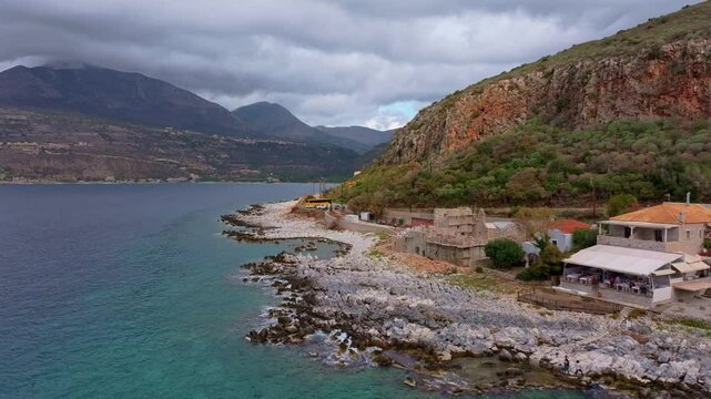 Aerial view of rocky coastline with a picturesque village and historic stone buildings by the Mediterranean Sea, Limeni, Greece.