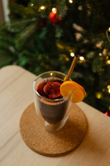 Closeup of a hand decorating mulled wine with orange slice, reusable golden straw, tree, and bokeh lights.