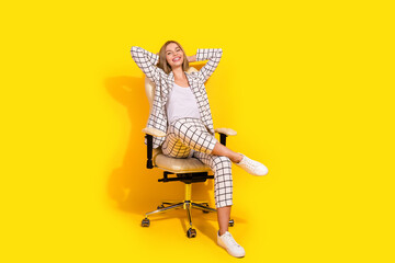 Young professional woman in elegant suit sitting relaxed on chair with yellow background, showcasing a perfect blend of business and casual style for advertising and work environments.