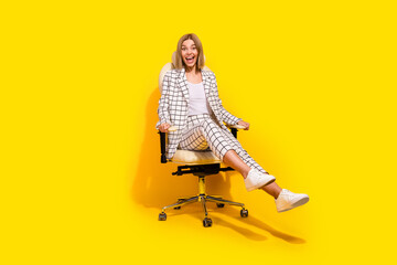 Confident young woman in stylish suit enjoys moment in office chair with vibrant yellow background
