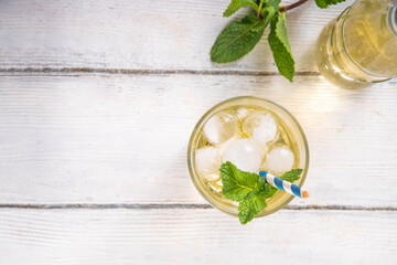 Cold vanilla cream soda drink. Tasty sweet non-alcohol beverage for hot summer days, with a lot of crushed ice and mint decor, on white wooden table copy space