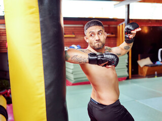 Male mixed martial arts fighter training with punching bag, practicing his punches wearing boxing...