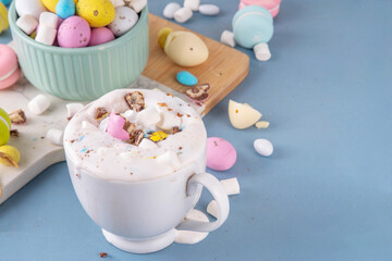 Easter hot chocolate with whipped cream, marshmallow and crushed chocolate mini eggs, on colorful table background, with ingredients, copy space