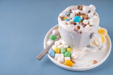 Easter hot chocolate with whipped cream, marshmallow and crushed chocolate mini eggs, on colorful table background, with ingredients, copy space