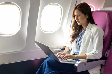 Fototapeta premium A woman is sitting on a plane with a laptop open in front of her. She is wearing sunglasses and she is working on her laptop 