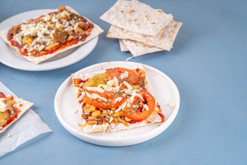 Matzah Pizza on light blue background with ingredients, cheese, tomato sauce. Food ideas and recipe for Jewish Pesach and Passover holidays