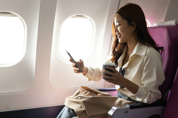 Fototapeta premium A woman is sitting on a purple airplane seat with a cell phone in her hand. She is smiling and she is happy 