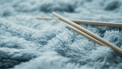 Close-up of knitting needles and light blue yarn against soft gray fabric, symbolizing cozy winter fun and craftsmanship.