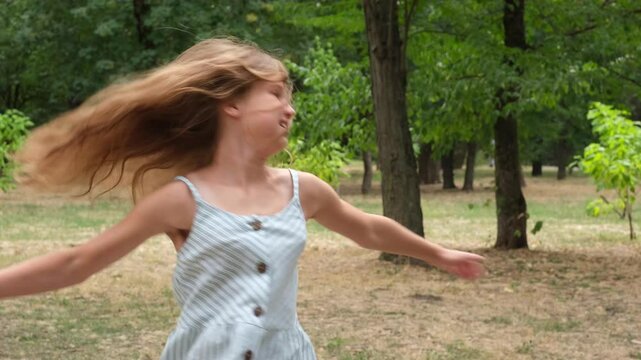 Preteen girl dancing and spinning, feeling happy in park summer day. Light long hair is developing. Childhood concept