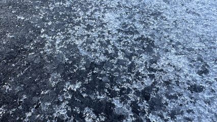 Detailed view of a frosty, textured surface covered in partially melted ice crystals, showcasing winter's intricate natural patterns