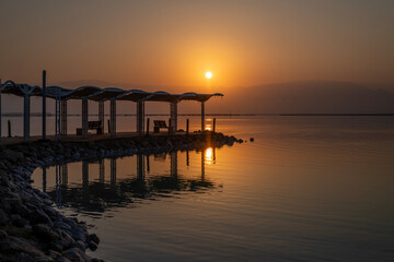 Shade structure with walkway and handrails with reflection in the water at the beach of the Dead Sea in Israel. 

