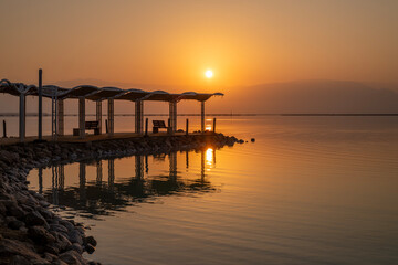 Fototapeta premium Shade structure with walkway and handrails with reflection in the water at the beach of the Dead Sea in Israel. 
