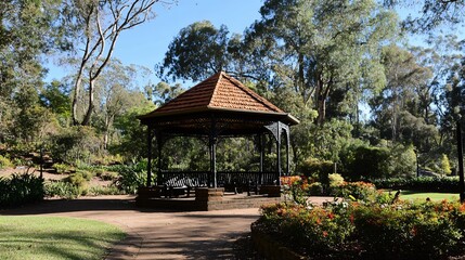Fototapeta premium Rustic gazebo in a park with lush greenery, flower beds, and pathways.