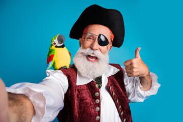 Photo portrait of old funny pirate male take selfie photo thumb up dressed carnival party costume party isolated blue color background © deagreez