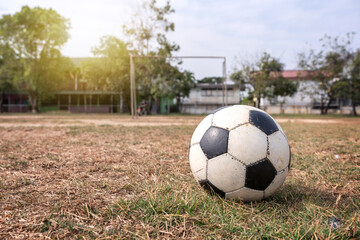 Fototapeta premium Dirty soccer ball on a very poor bad grass. Old country style football field in School Local Thailand with the light in the evening atmosphere have background copy space.