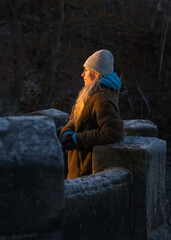 Tourist girl in warm clothes stands o Bastay Bridge in Saxon Switzerland at sunset, admiring view of majestic cliffs. Last ray of light falls on her face. Popular tourist destination. Germany.