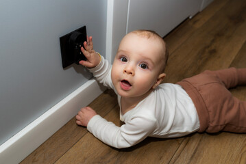 A seven-month-old Caucasian baby touches a black electrical outlet on the wall.