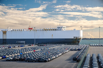 Large cargo ship docked near a vast parking lot of vehicles