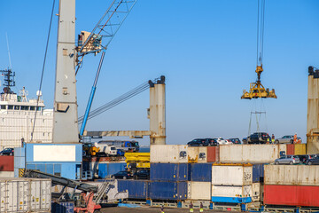 Port crane loading car into containers on bull carrier in port on