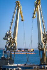 Distant container ship between two floating port cranes on a sunny day