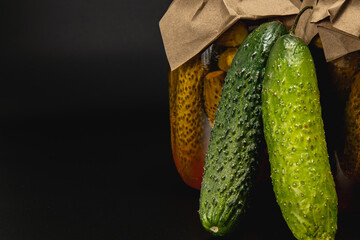 Homemade pickled cucumbers and tomatoes in jars on a dark background