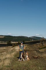 Young woman with a backpack and two dogs travels in the fields in the mountains of southwestern Serbia near Zlatibor town. Hiking in nature in early autumn on a sunny, warm day. Front view portrait.