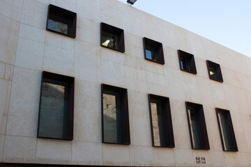 Edificio moderno con ventanas rectangulares de color oscuro dispuestas en diagonal sobre na fachada de color claro.