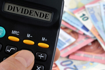 Calculatrice affichant dividende posée sur des billets de banque en euro flous