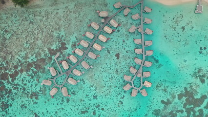 Aerial view of luxurious overwater bungalows in vibrant turquoise lagoon, creating a breathtaking tropical island paradise, inviting relaxation and escape. Remote wild nature, exotic summer travel