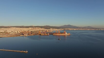 Thessaloniki, Greece - 01 December 2024: Aerial view of port at sunset with Aegean Sea and cityscape surrounded by mountains, Thessaloniki, Greece.