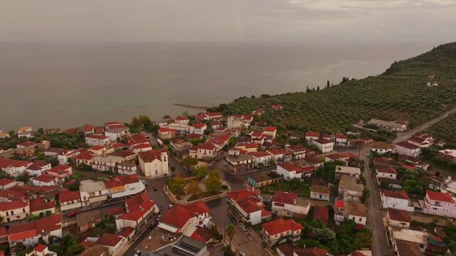 Aerial view of a beautiful village with scenic rooftops and olive trees overlooking the Ionian Sea at sunset, Nea Koroni, Greece.