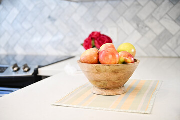Wooden bowl filled with fresh apples on a countertop near a stove.