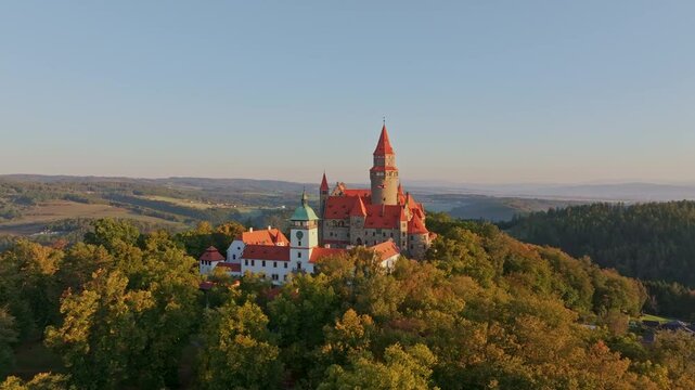 Aerial view of Bouzov Castle at sunrise surrounded by hills and forest, Bouzov, Czech Republic.